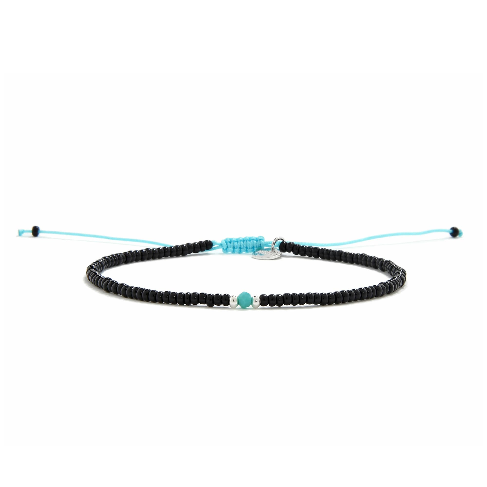 A straight-on view of an adjustable beaded bracelet with black beads, a turquoise bead, and a bright blue cord on a white surface.