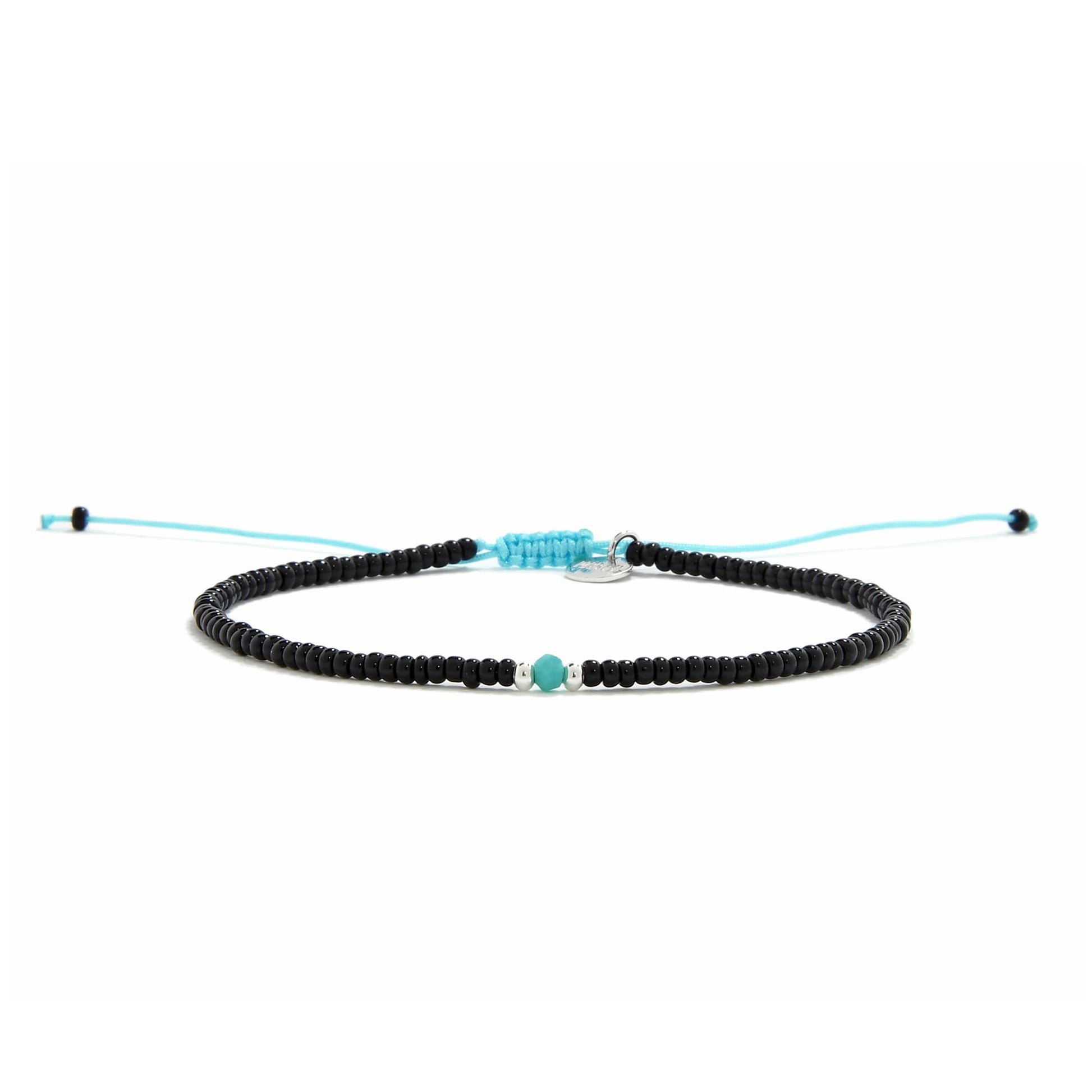 A straight-on view of an adjustable beaded bracelet with black beads, a turquoise bead, and a bright blue cord on a white surface.