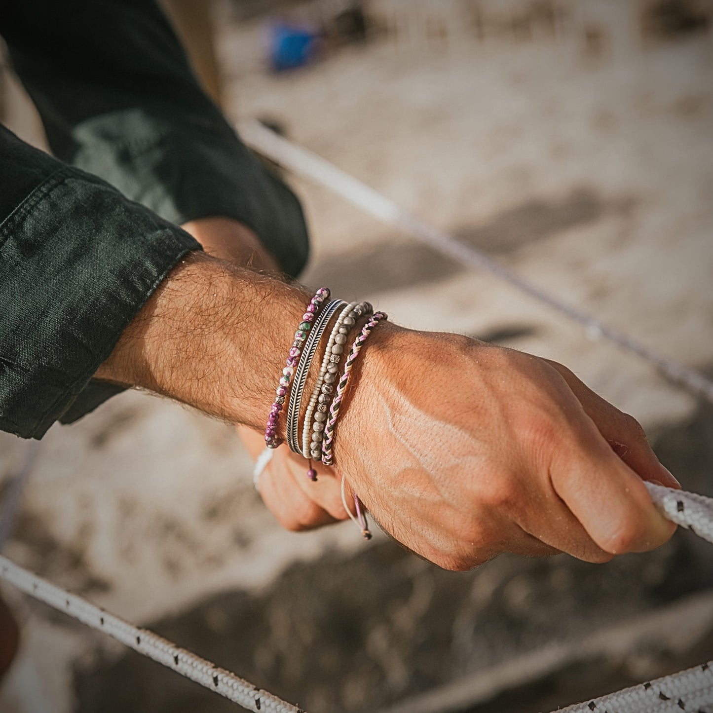 Men's hand on rope, styled with the Amalfi bracelet stack in muted coastal colors.