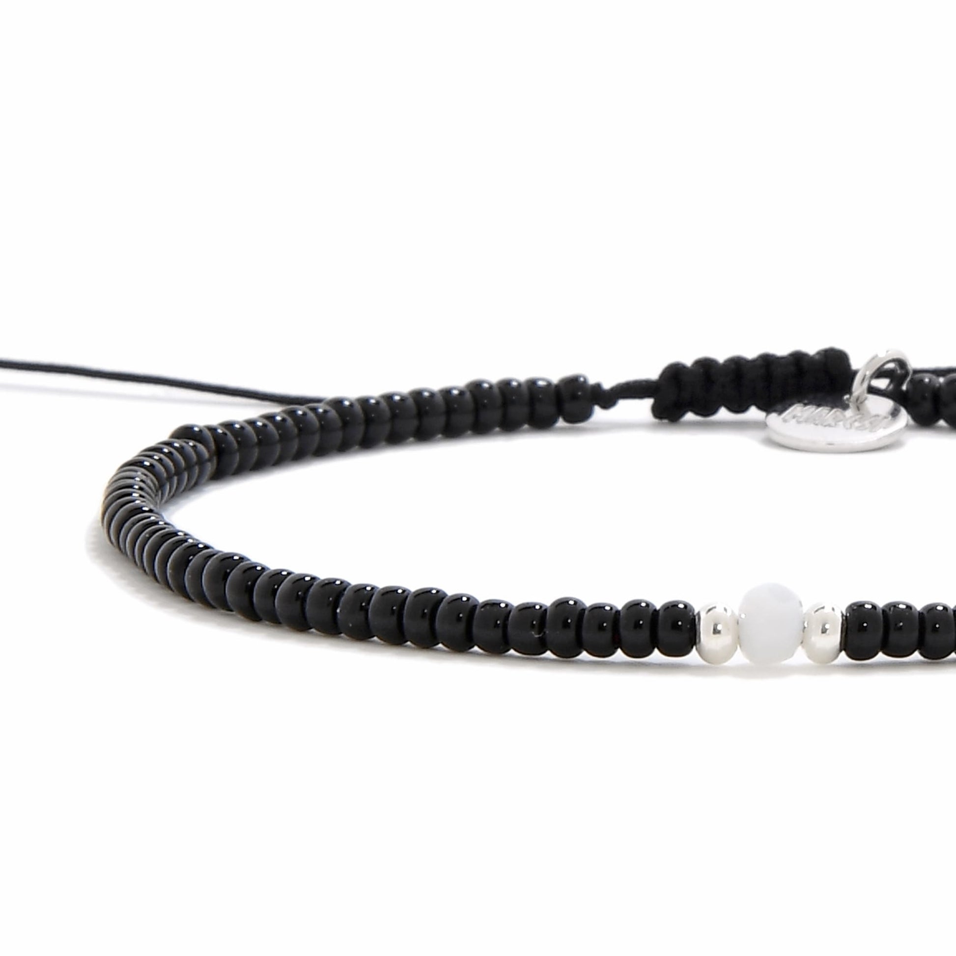 A detailed, angled view of a bead bracelet black with a matte white bead and two silver accent beads.