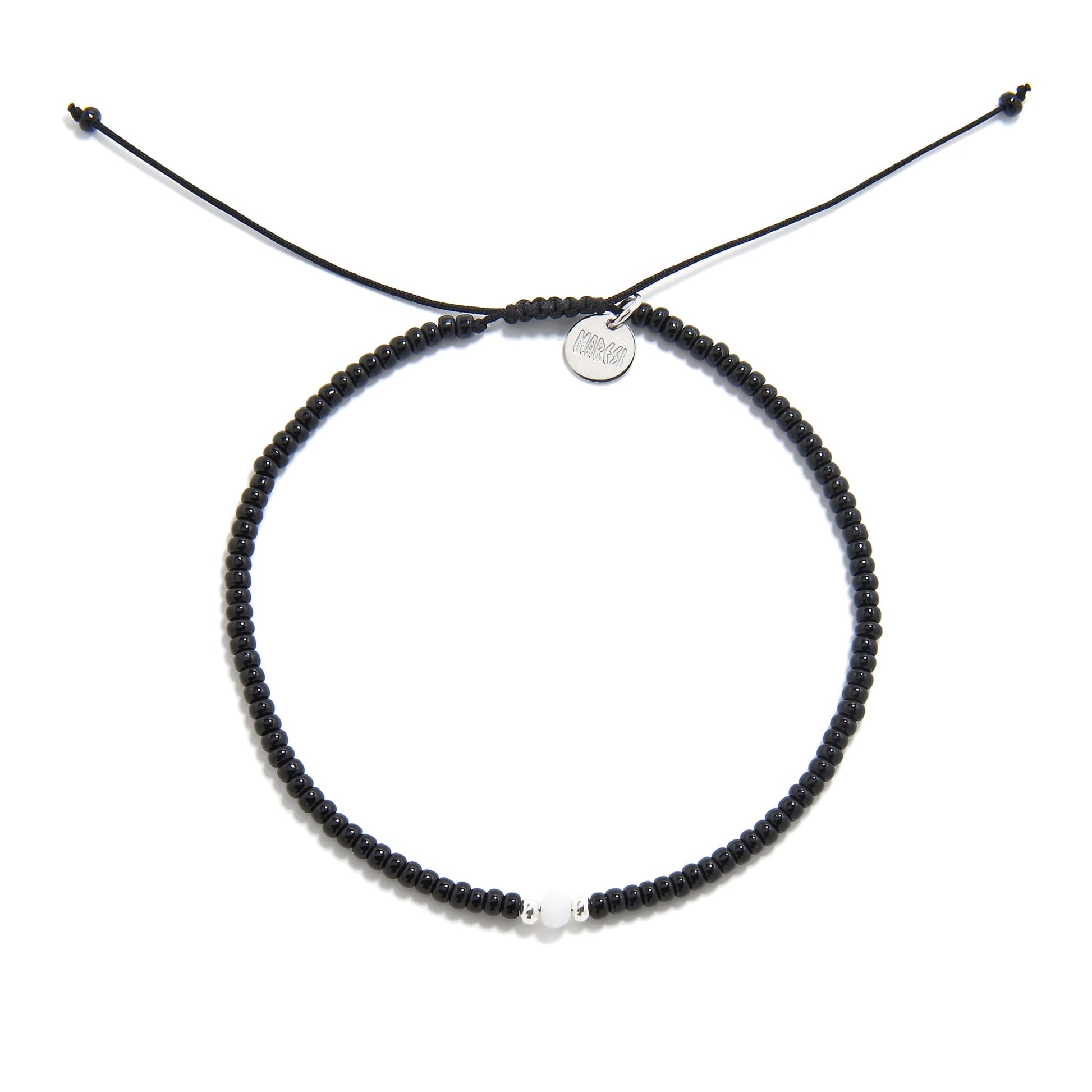 A top-down shot of a round bead bracelet black featuring a single white bead, a silver charm, and an adjustable cord.