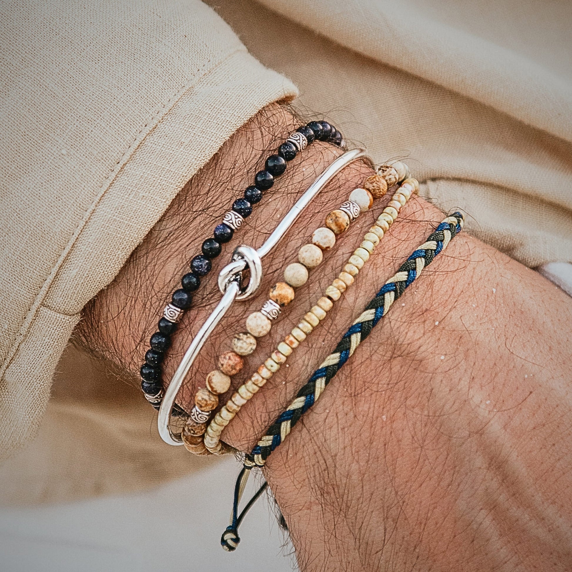 Beige shirt and arm adorned with five layered Capri-style bracelets.