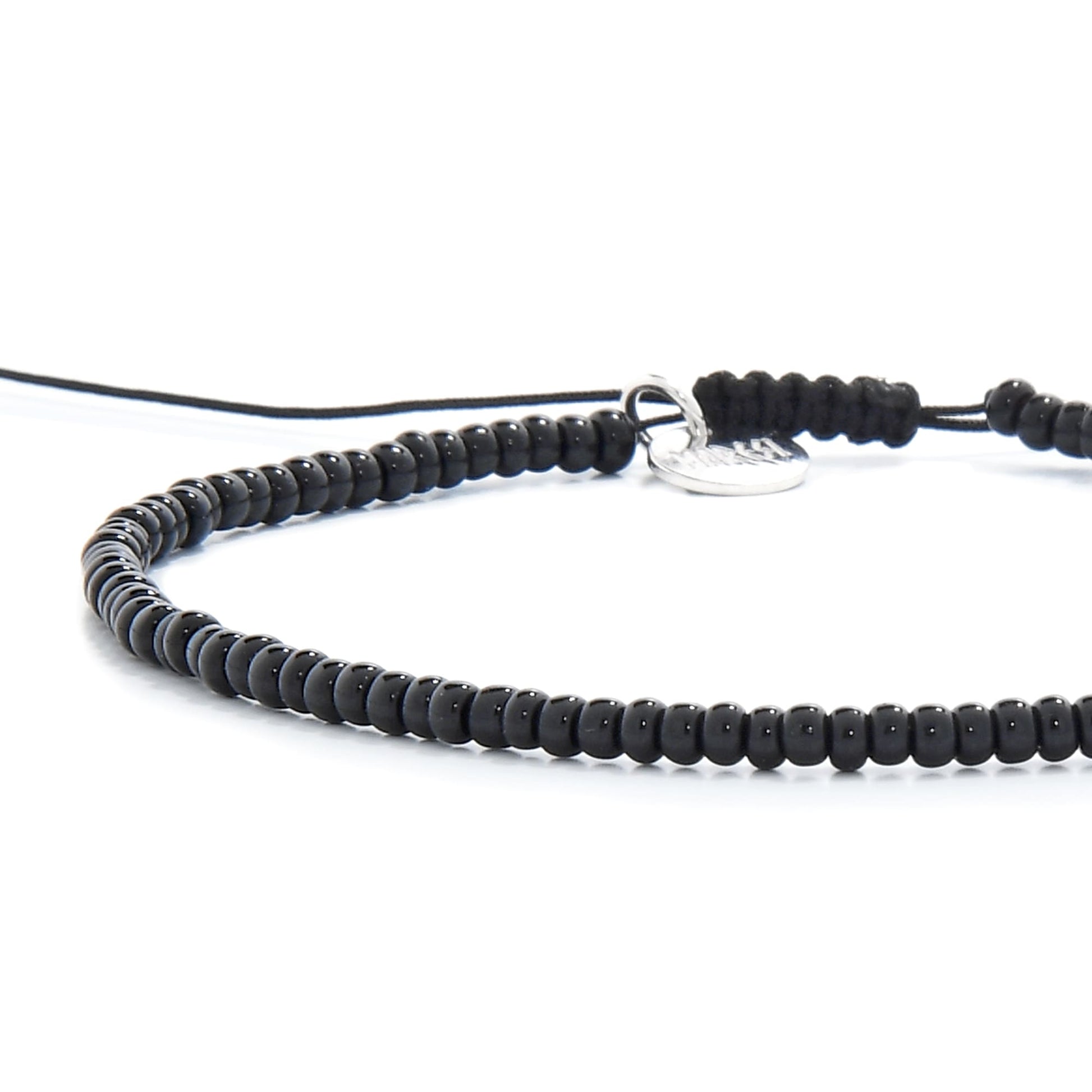 An extreme close-up of a black bead bracelet, focusing on the small, uniform beads and the engraved silver charm.