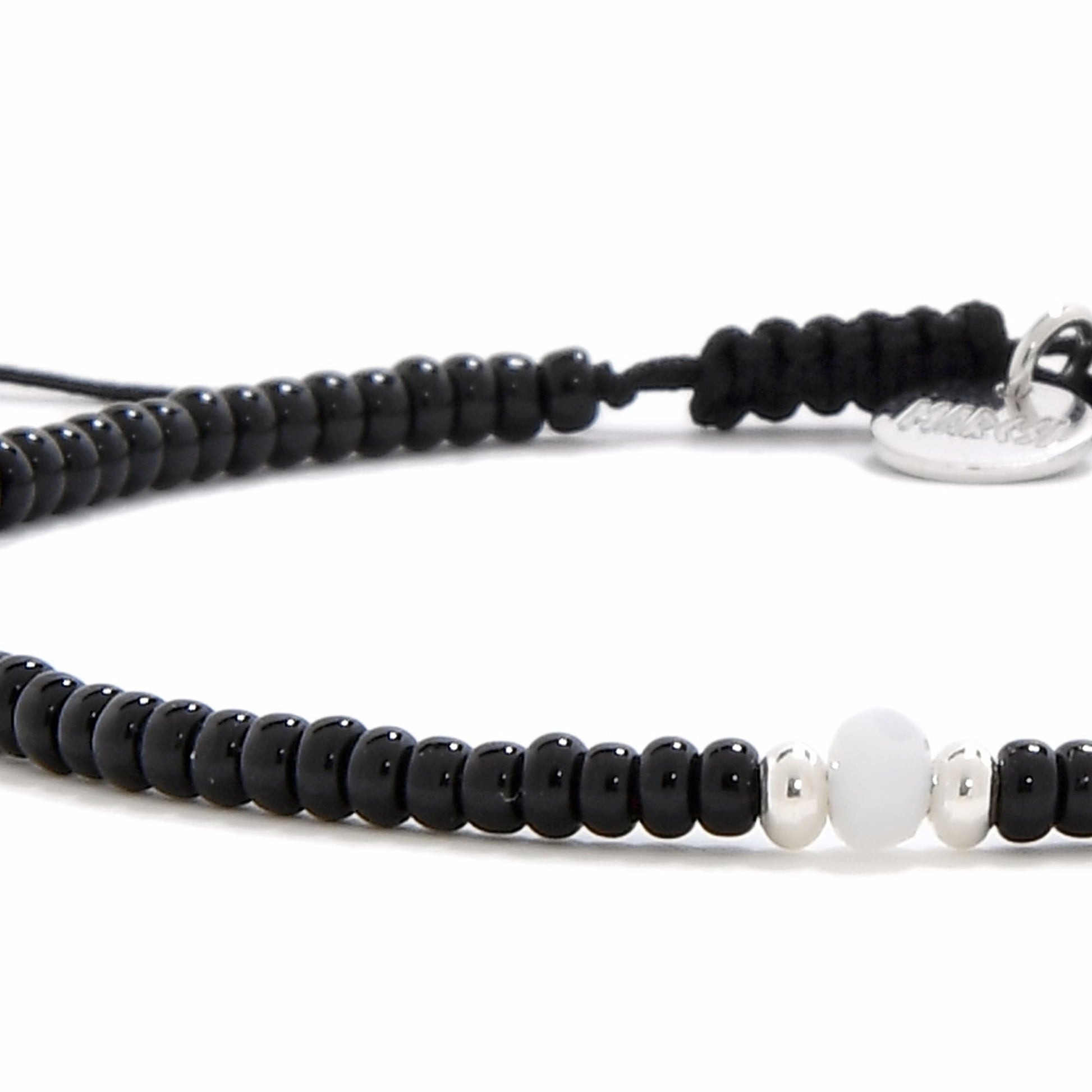 An extreme close-up of a bead bracelet black, highlighting the smooth white bead and two small silver beads in the center.
