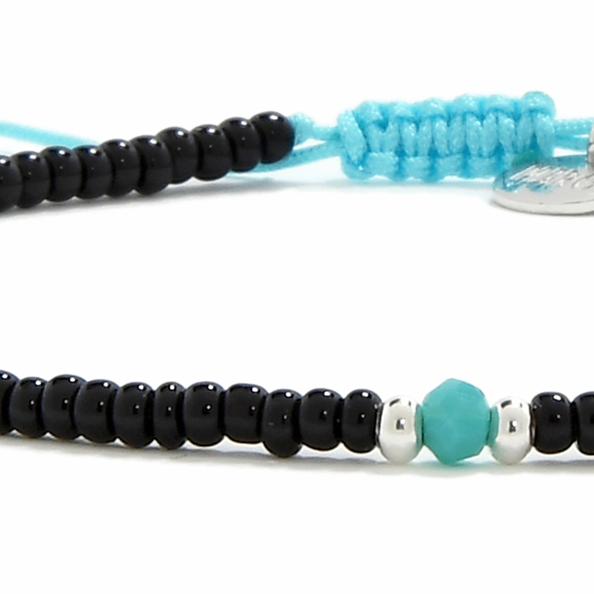 An extreme close-up of a beaded bracelet highlighting the faceted turquoise bead and two shiny silver beads.