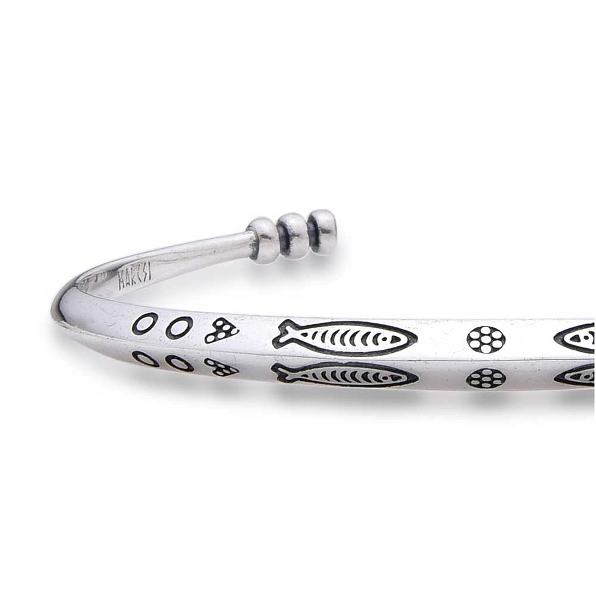 Close-up of cuff bracelet showing fish and circle engravings