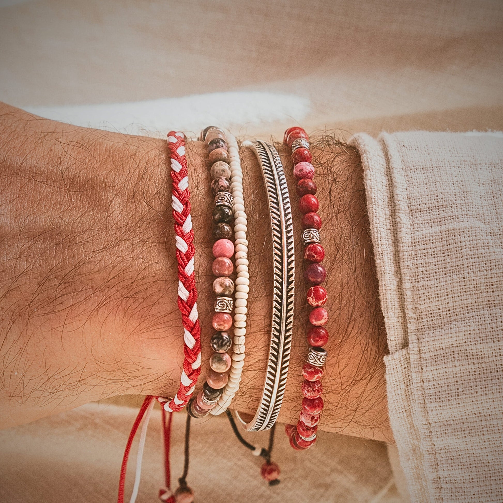 Handmade friendship bracelet in red and white stacked with bead and metal bracelets on wrist