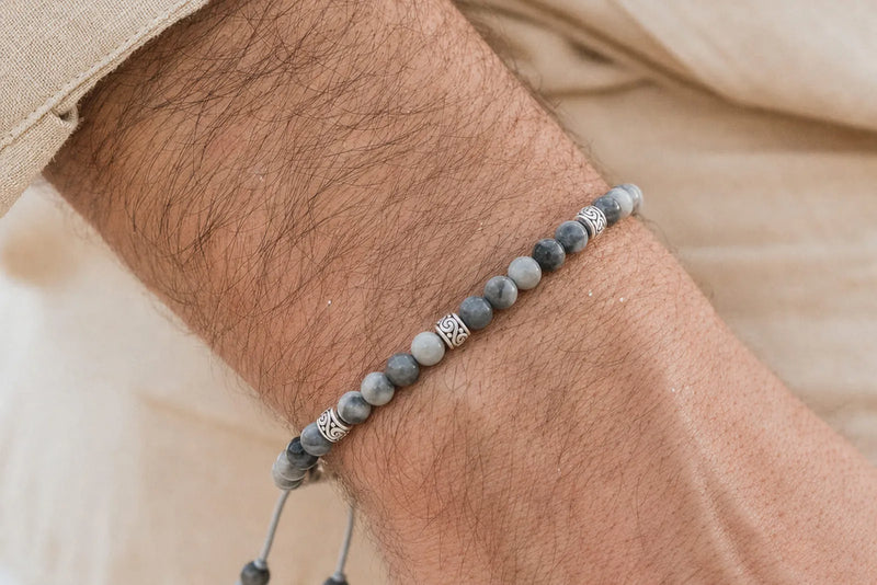 Gray beaded bracelet with marbled stone beads and silver spacers worn on a man’s wrist in a warm neutral setting.