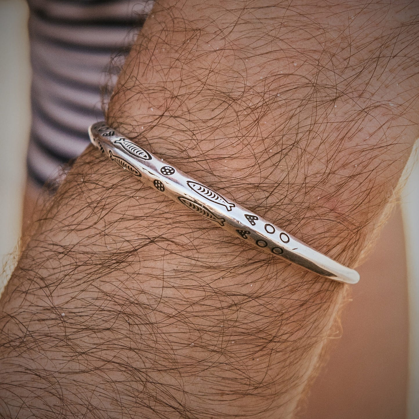 Men’s cuff bracelet in metal with fish engraving worn on wrist