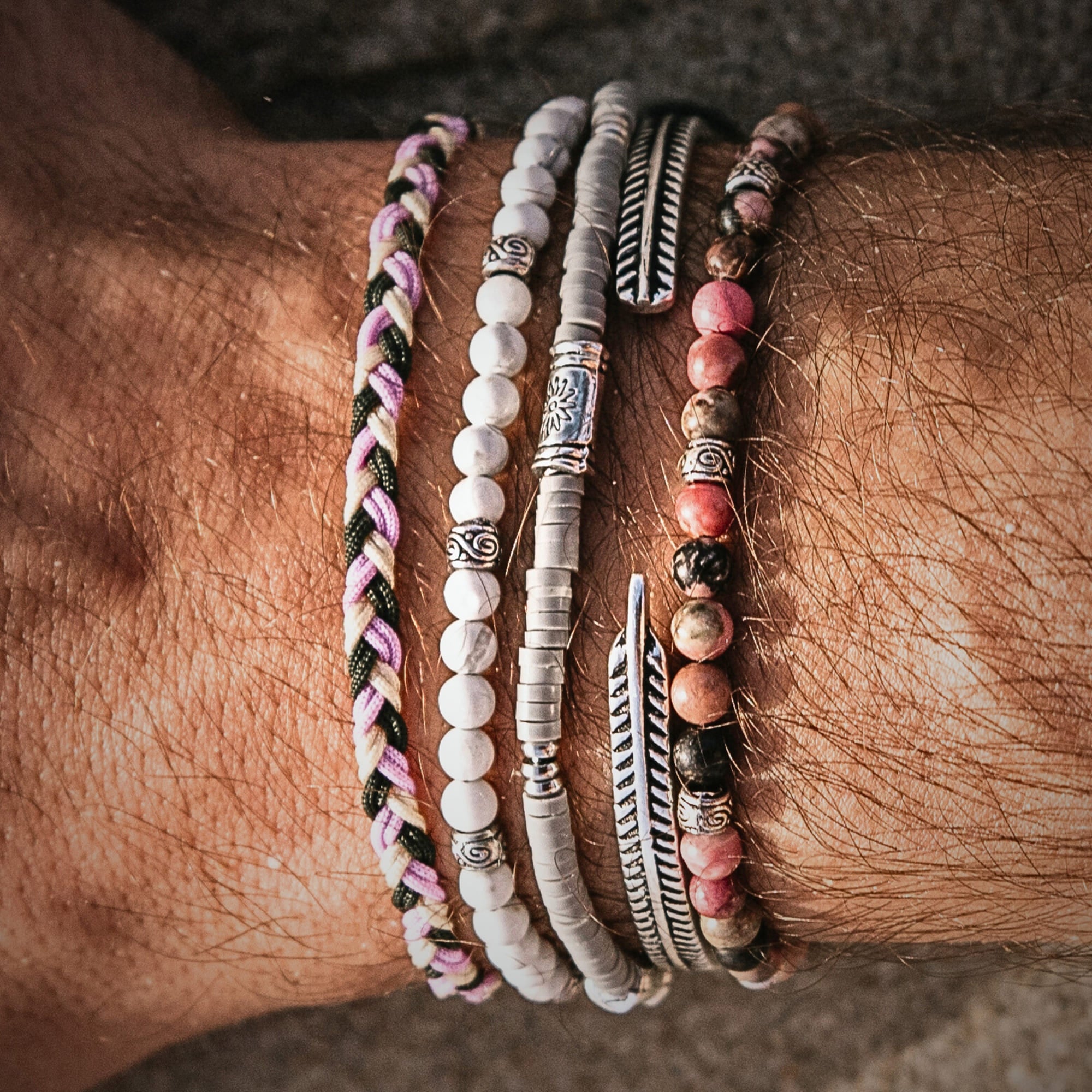 Stacked Mallorca bracelet set featuring braided cord, white and pink beads, and silver elements on a male wrist at the beach