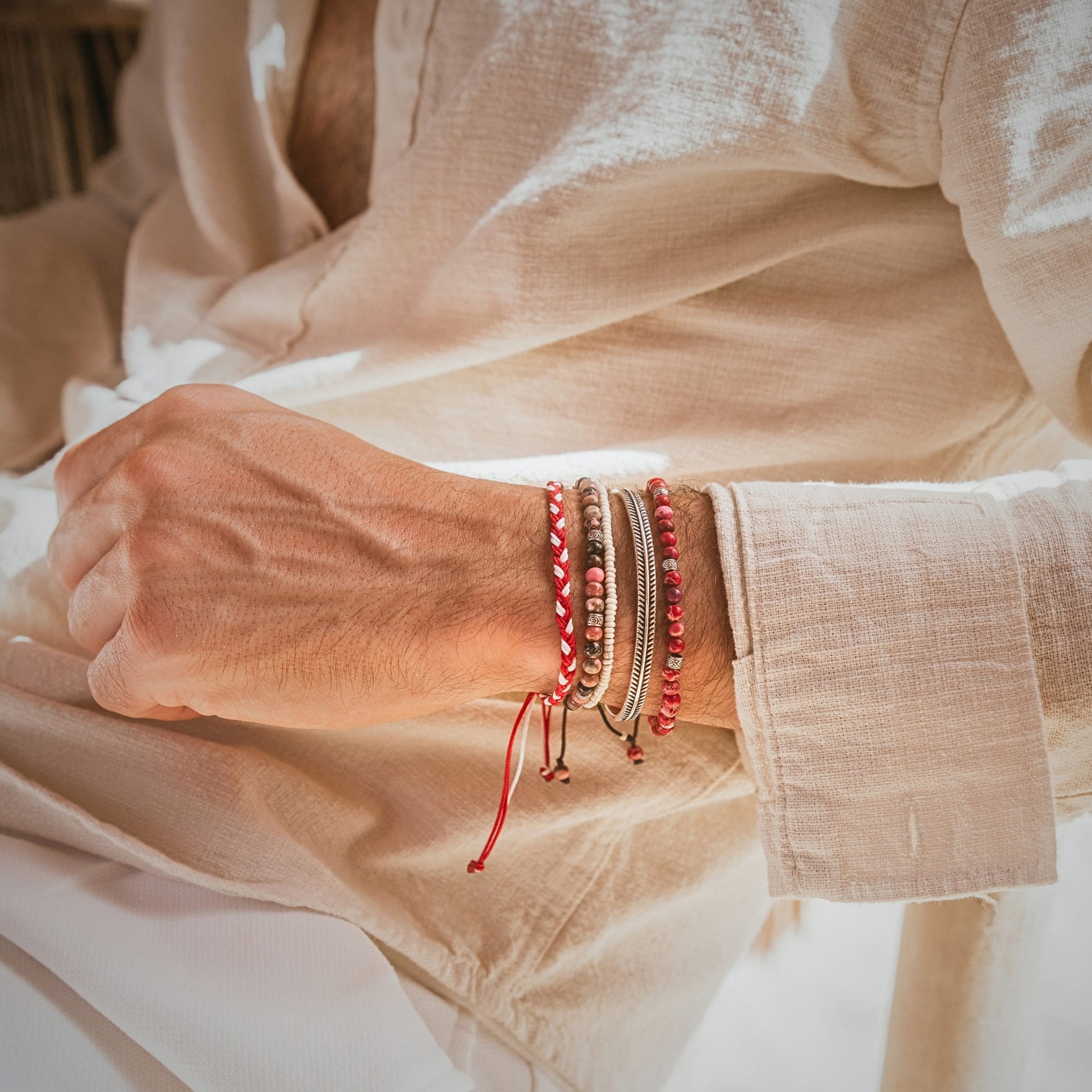 Man wearing Marseille bracelet set with red and natural-toned stacks bracelets