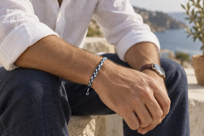 Man wearing a slim blue and white woven friendship bracelet with a white linen shirt and navy trousers.