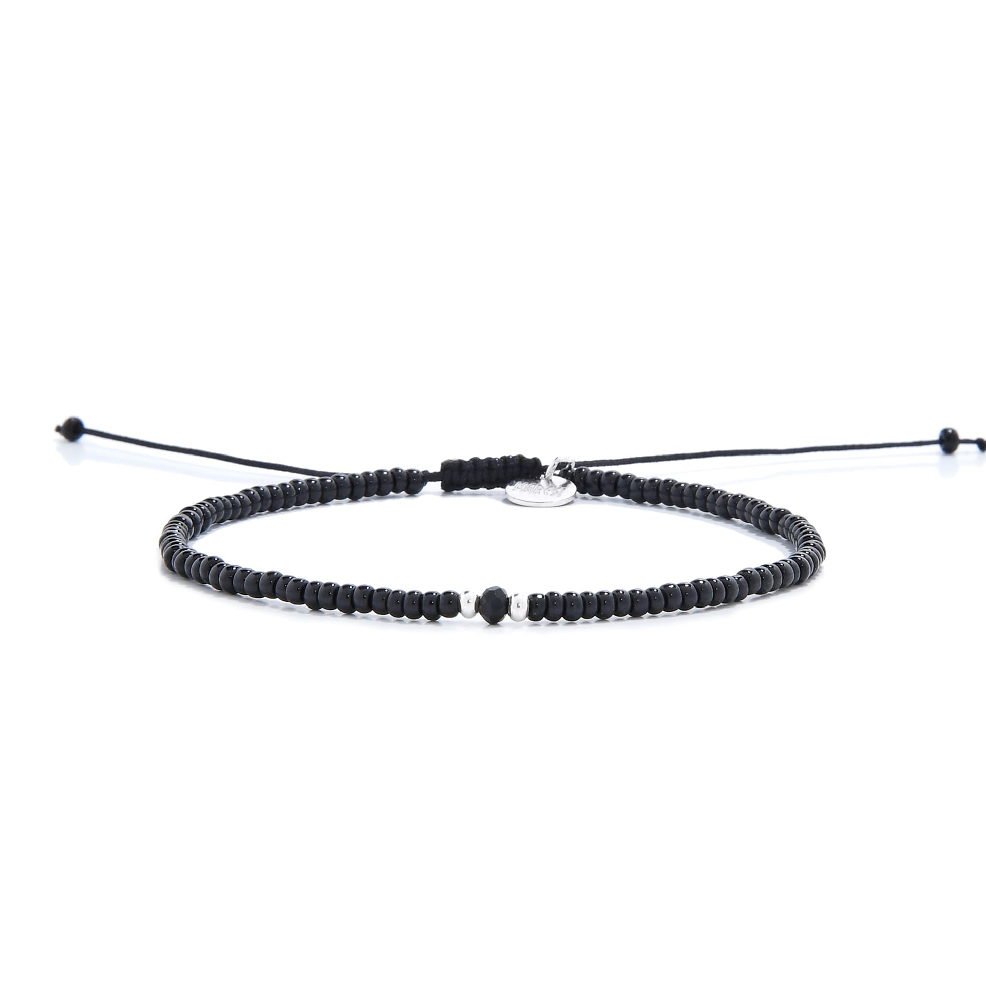 A mens beaded bracelet with glossy black beads, a faceted onyx bead, and a silver charm.