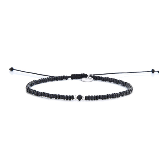 A mens beaded bracelet with glossy black beads, a faceted onyx bead, and a silver charm.