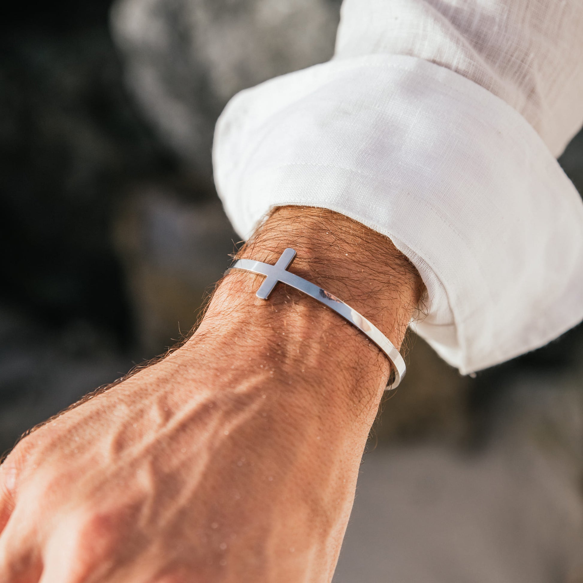 Stylish cross bracelet in silver, worn with casual white shirt.