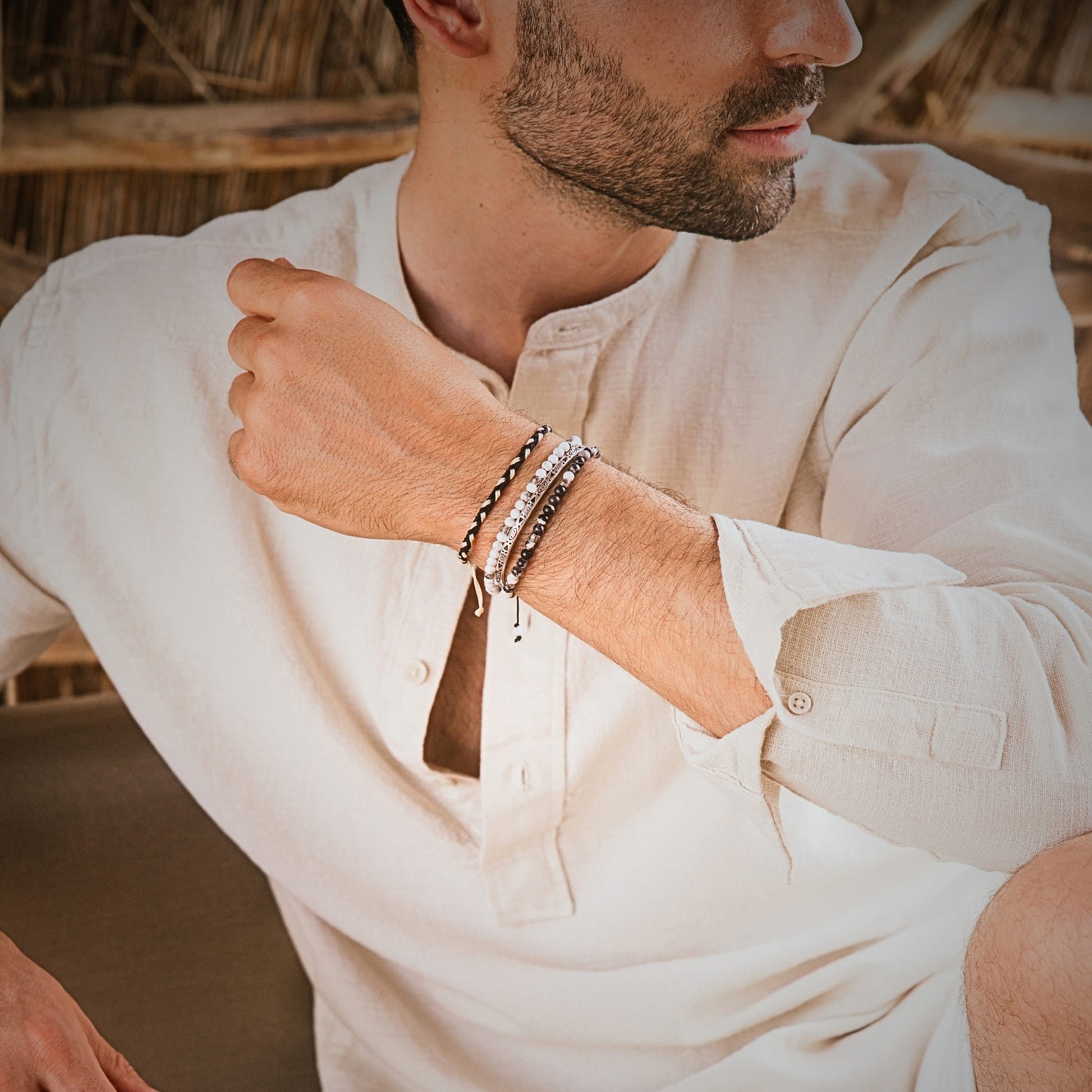 Man wearing Palma bracelet stack with natural outfit, sitting outdoors