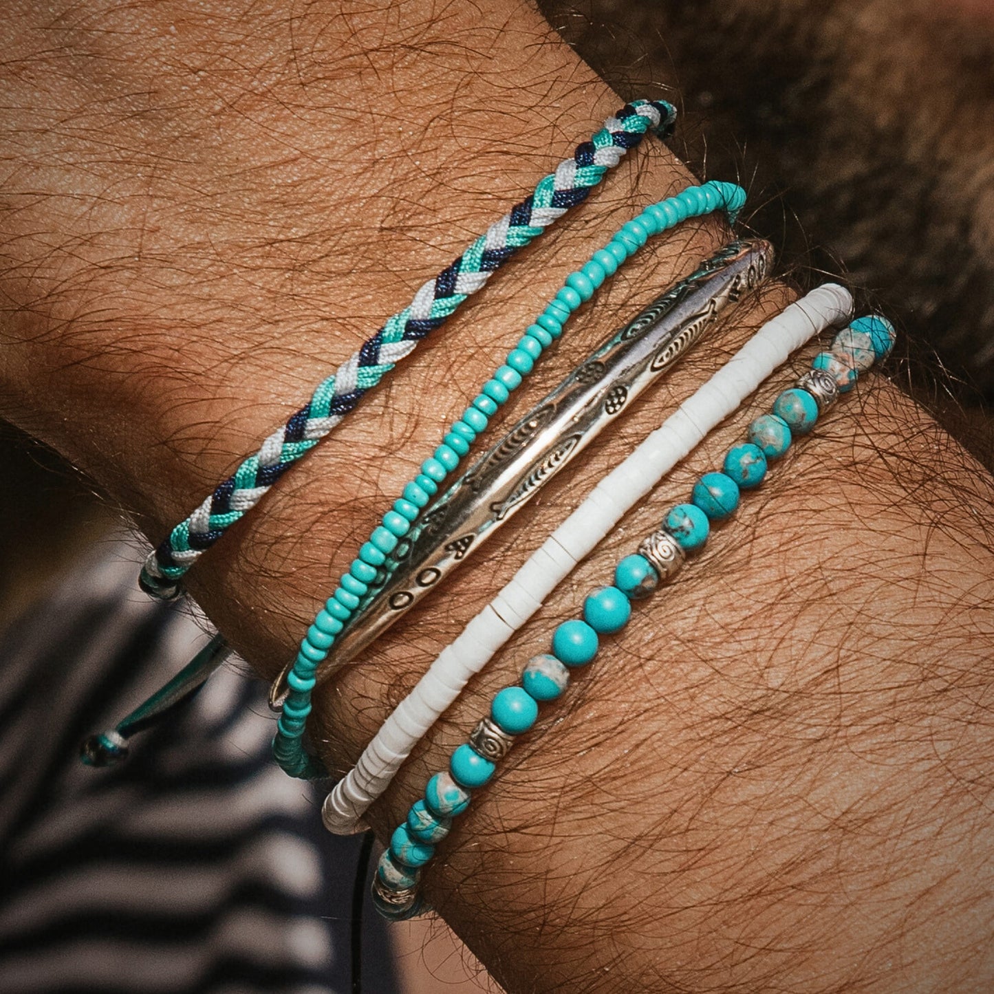 Wrist wearing six stacking bracelets in shades of turquoise, white, and silver, showcasing variety and texture in a coordinated set.