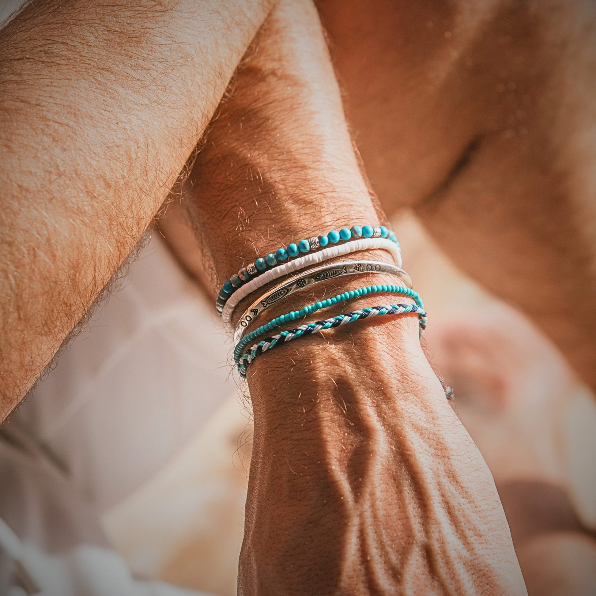Man wearing Positano stacking bracelets with turquoise beads, white accents, and silver bangles.