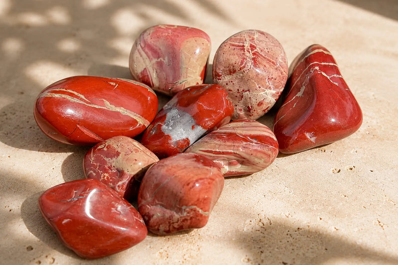 Polished red jasper stones with cream veins, pale patches, and varied red patterns.