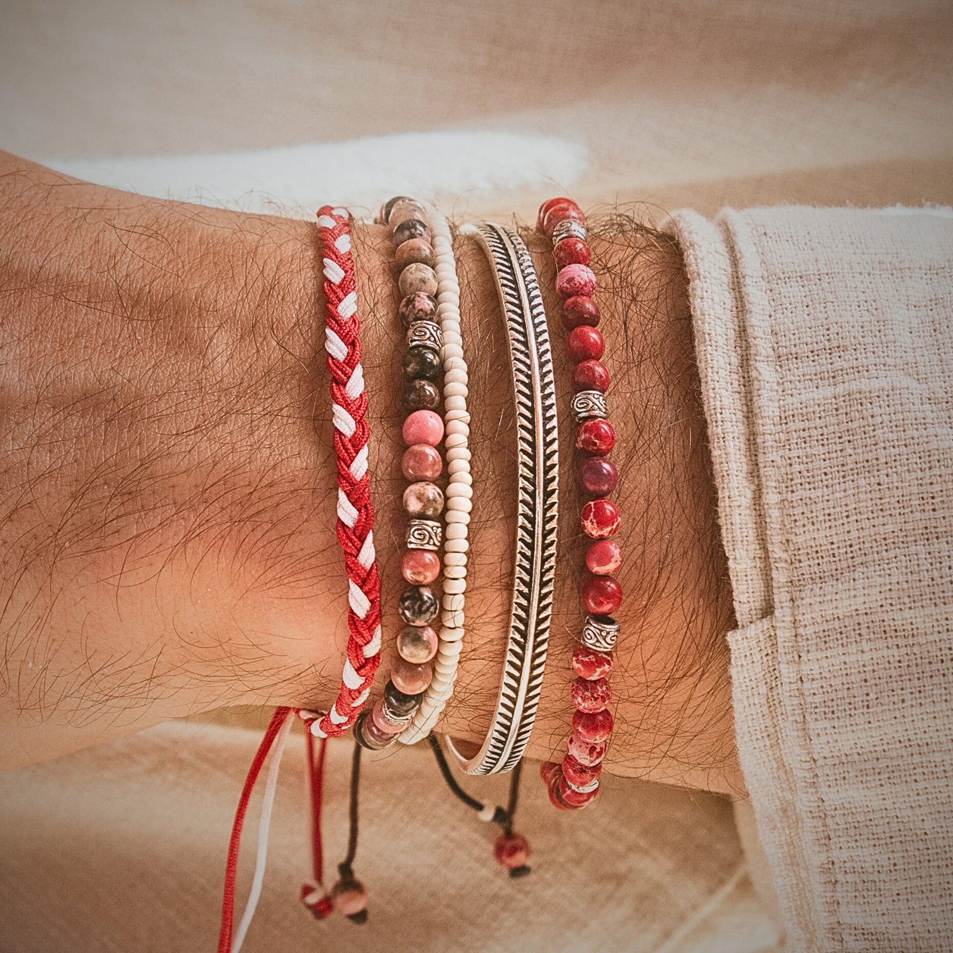 Red jasper bracelet styled on wrist in a layered bracelet set with red, white, and metallic accessories.