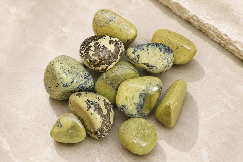 Jadeite vs Nephrite identification guide featuring polished yellow green serpentine stones with dark markings.