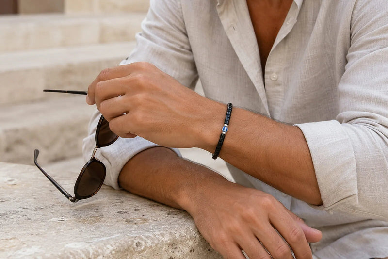 Man wearing a slim black bracelet with a white linen shirt in a relaxed Mediterranean setting