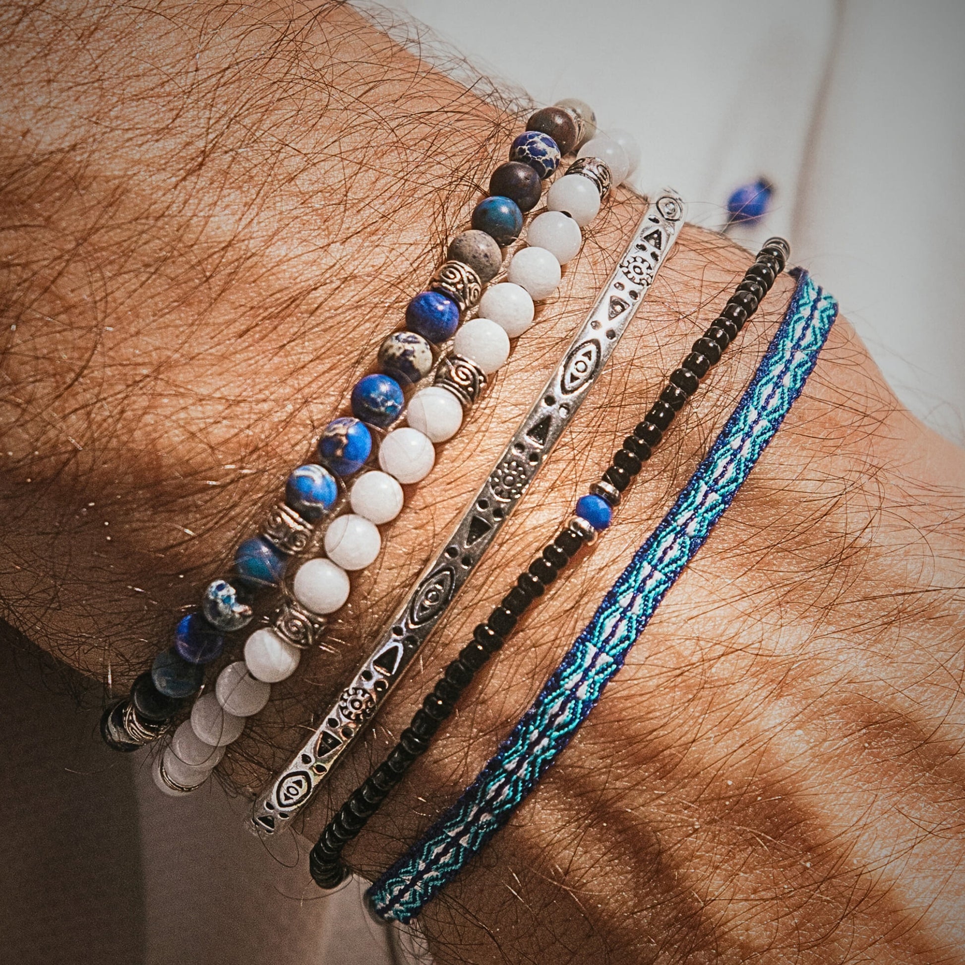 Stylish white jade stone bracelet stacked with blue and silver bracelets on a wrist.