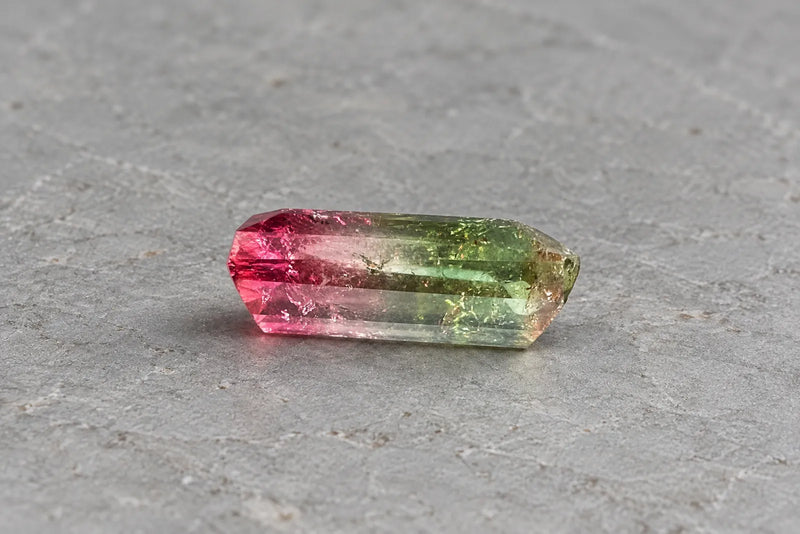 Colorful gemstones: pink and green tourmaline Elongated tourmaline with pink and green color zones on pale stone