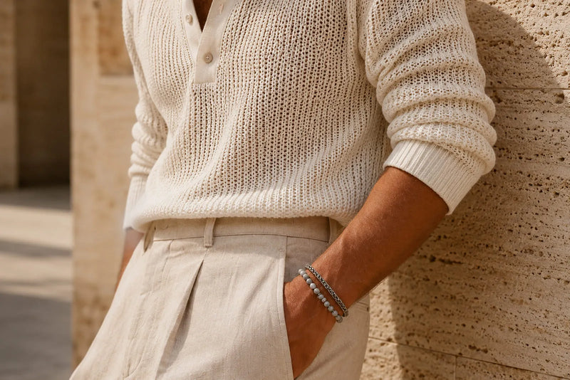 Man wearing a cream textured knit top, tailored trousers and a subtle bracelet as part of an elegant smart casual look.