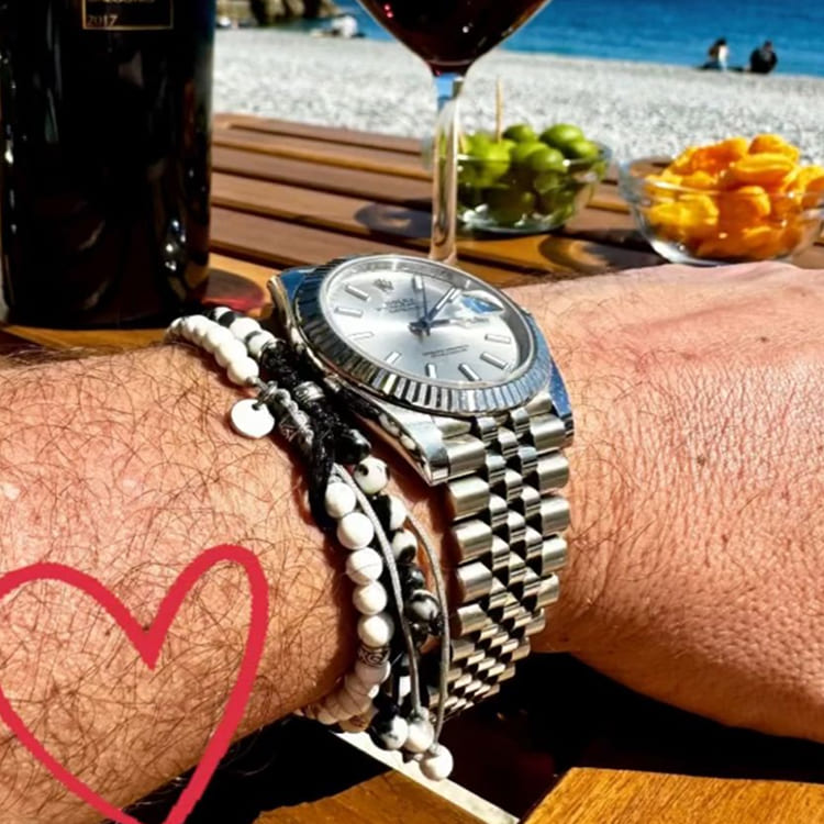 Silver watch on a wrist with a heart drawn on skin, beach setting in the background