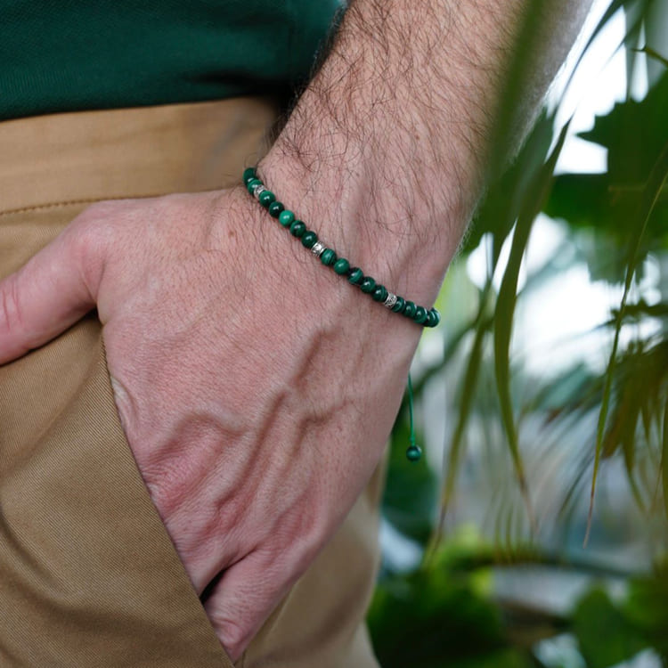 Close-up of a wrist wearing a green beaded bracelet with a blurred natural background