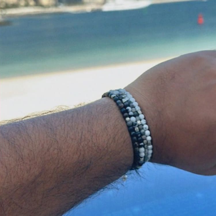 Close-up of a wrist wearing a beaded bracelet with a beach in the background