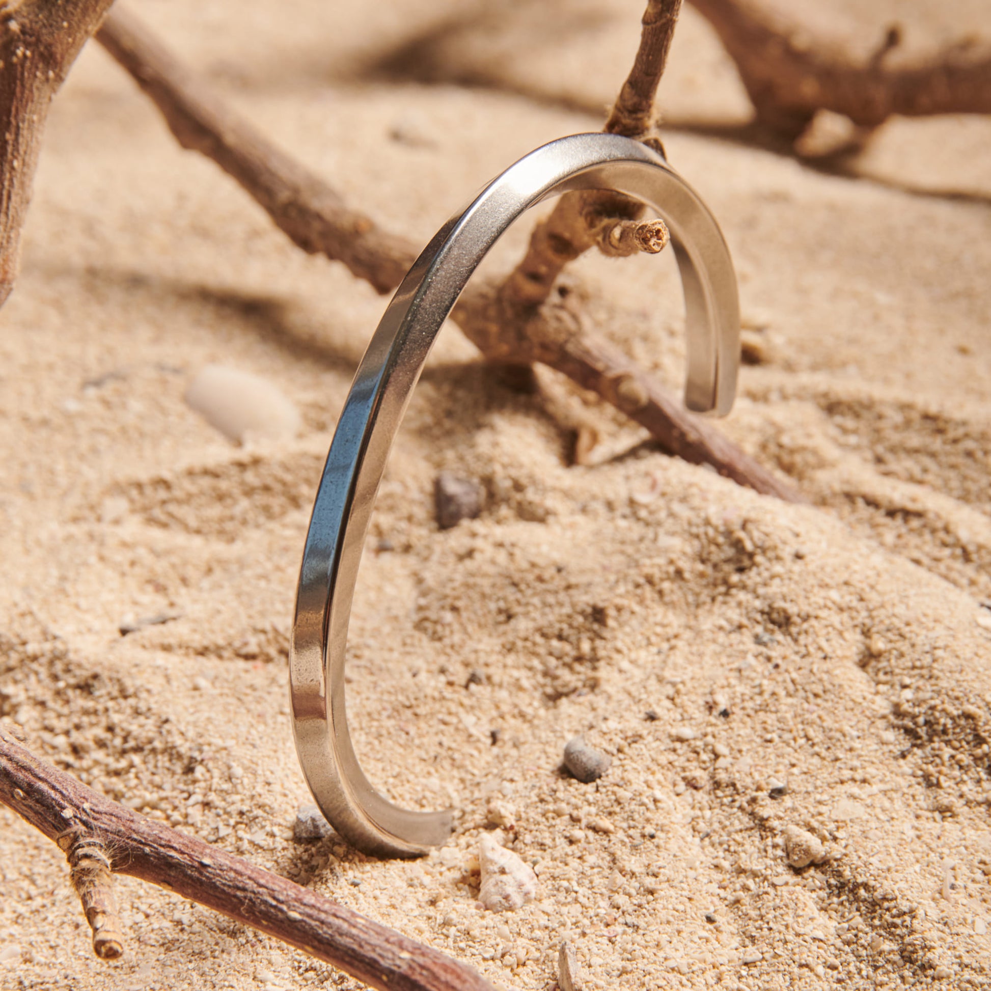 Minimal metal bangle for men standing on textured beach sand