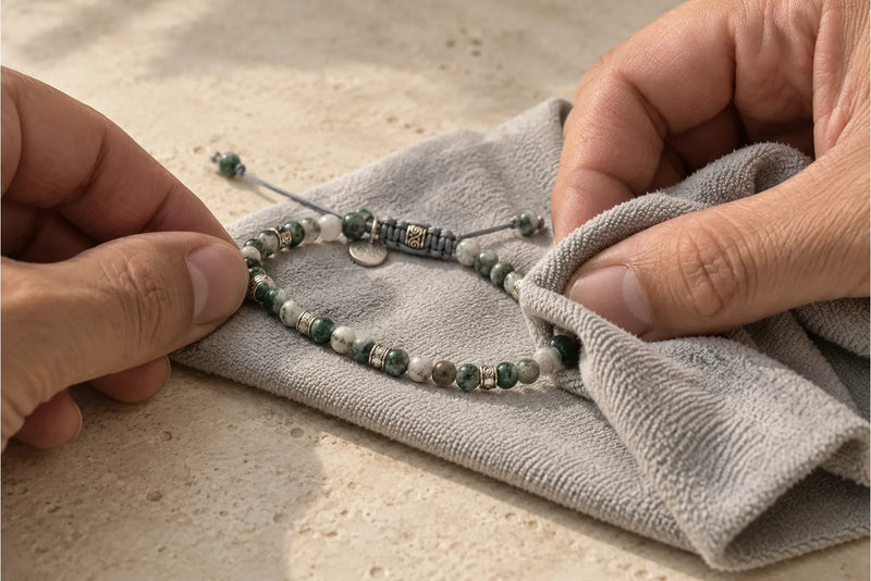 Moss Agate Bracelet Care with a Soft Cloth Hands gently wiping a green-and-white moss agate cord bracelet with a soft gray cloth.