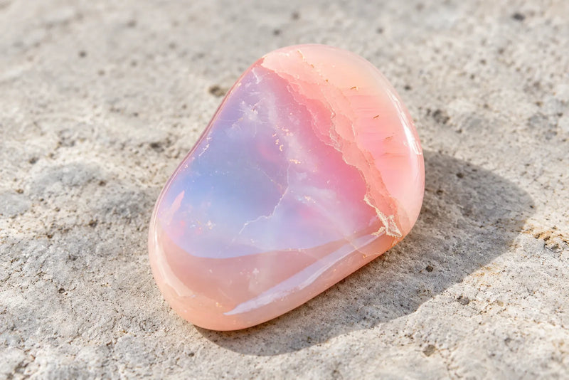 Pink opal: polished pastel stone Polished pink opal with peach-pink edges and a pale blue-gray area across its face.