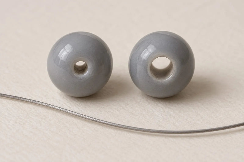 Stringing Beads: two gray round beads with different hole sizes beside a length of beading wire.