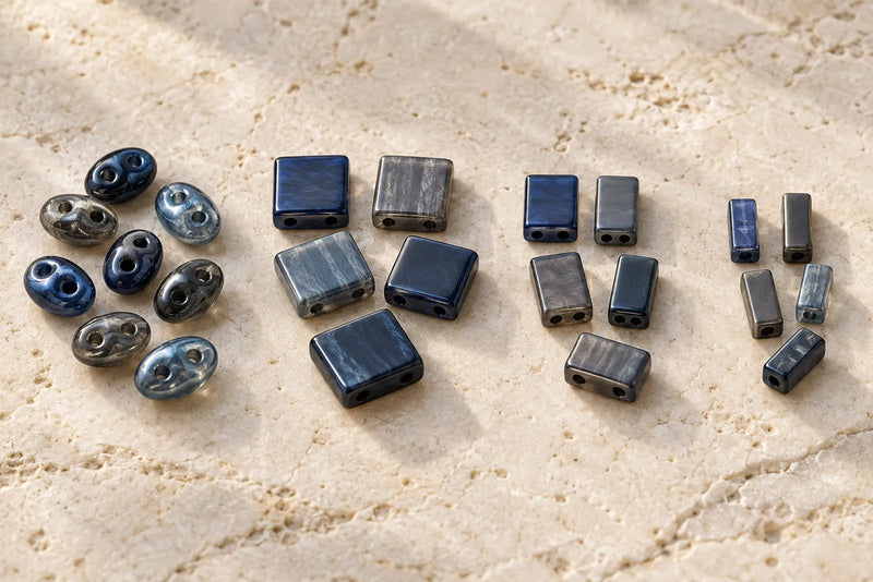 Types of Seed Beads shown as blue and gray two-hole oval, square, and rectangular beads on pale stone.