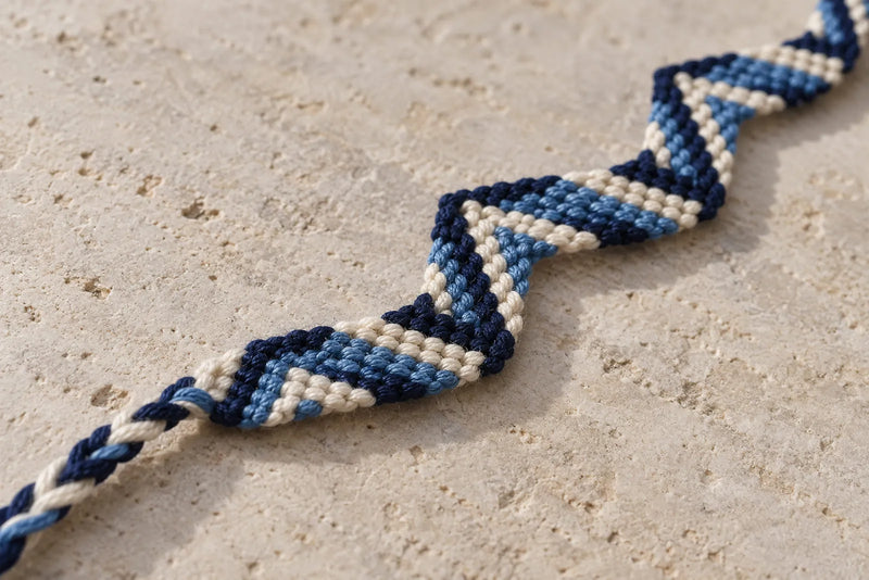Zig Zag Friendship Bracelet: Texture and Angled Edges Close-up of a navy, ivory, and blue zig zag friendship bracelet on pale stone, showing its angled edges.