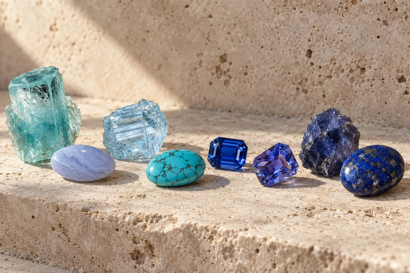 Blue gemstone names represented by aquamarine, turquoise, sapphire, tanzanite, iolite and lapis lazuli on warm travertine.