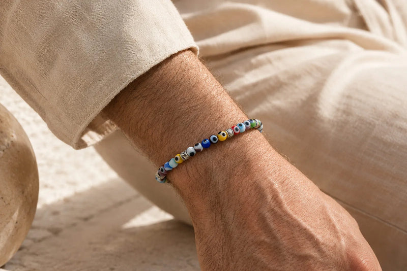 Evil eye bracelet on a man’s wrist, styled with beige linen in a warm Mediterranean setting.