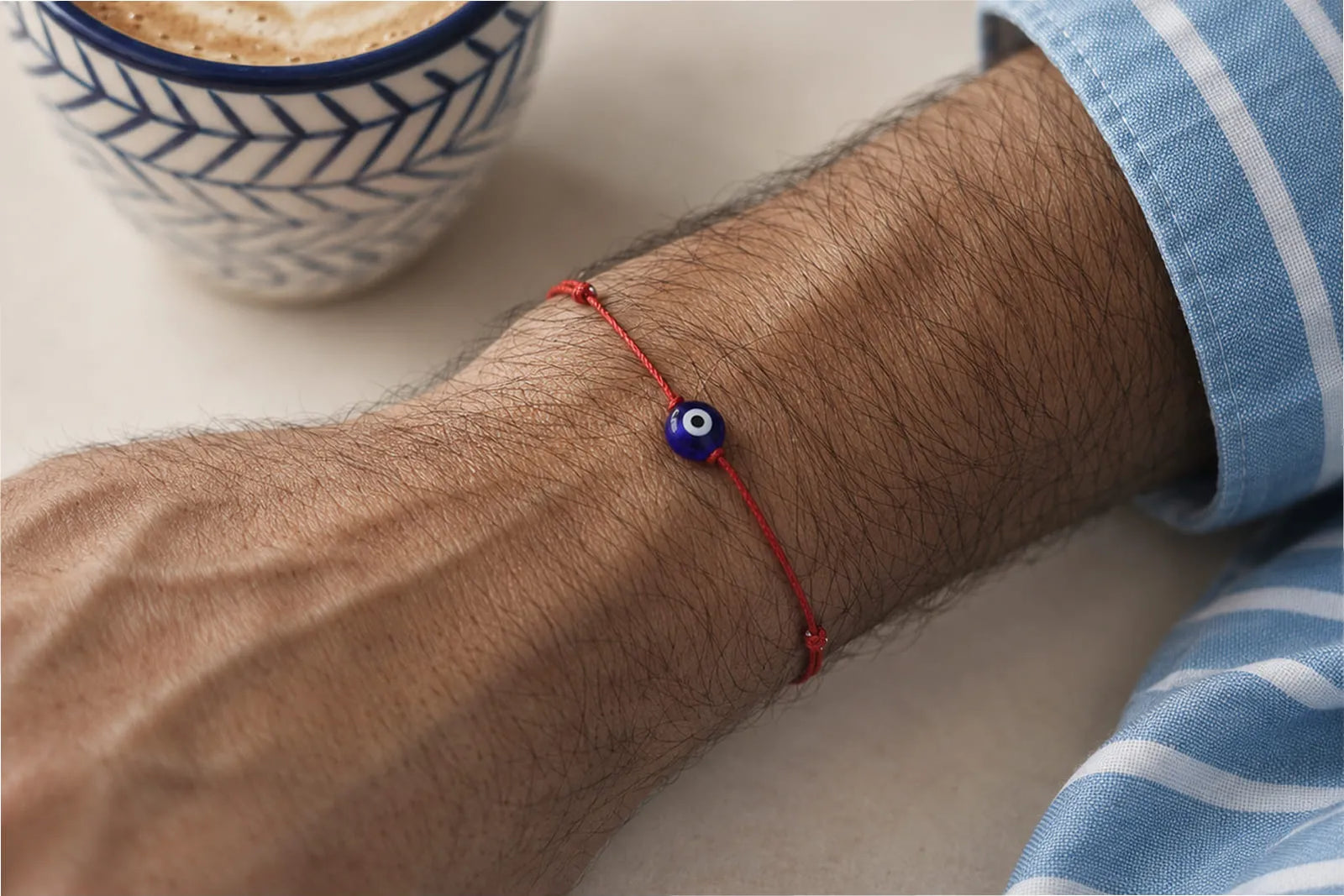 Evil Eye Bracelets Meaning, shown with a blue evil eye bead on a red cord bracelet worn by a man.