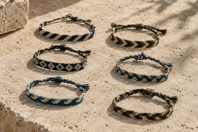 Six men’s friendship bracelets with striped, diamond, and wave patterns arranged on warm travertine stone.