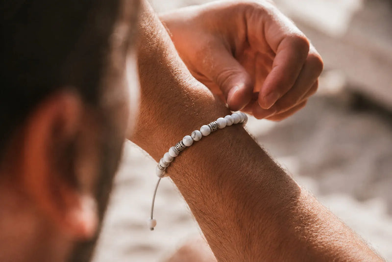 Gemstone bracelet fit shown on a man’s wrist as he adjusts a white beaded bracelet with silver details.