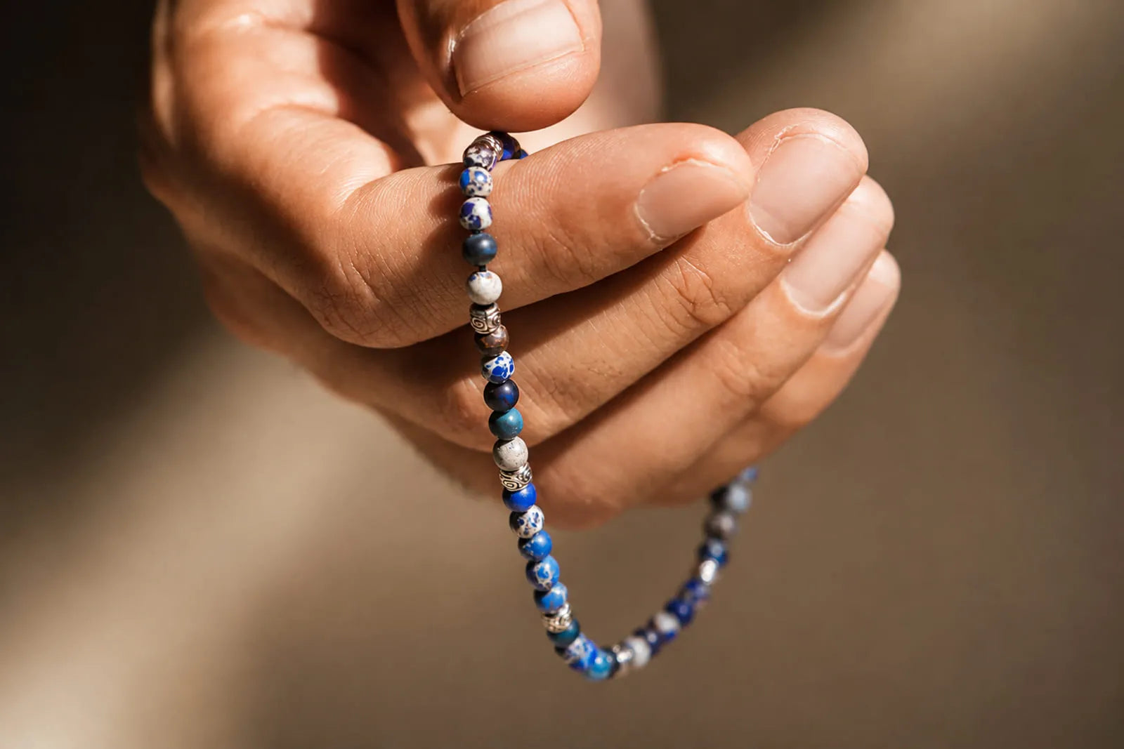 Gemstone bracelet with blue stone beads and silver spacers held naturally in a man’s hand under warm sunlight.