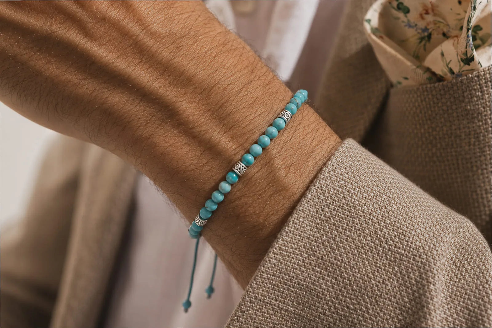 Genuine turquoise bracelet with metal spacers worn on a man’s wrist with a beige textured blazer.