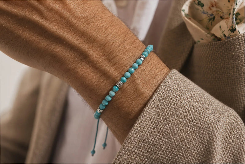 Genuine turquoise bracelet with metal spacers worn on a man’s wrist with a beige textured blazer.