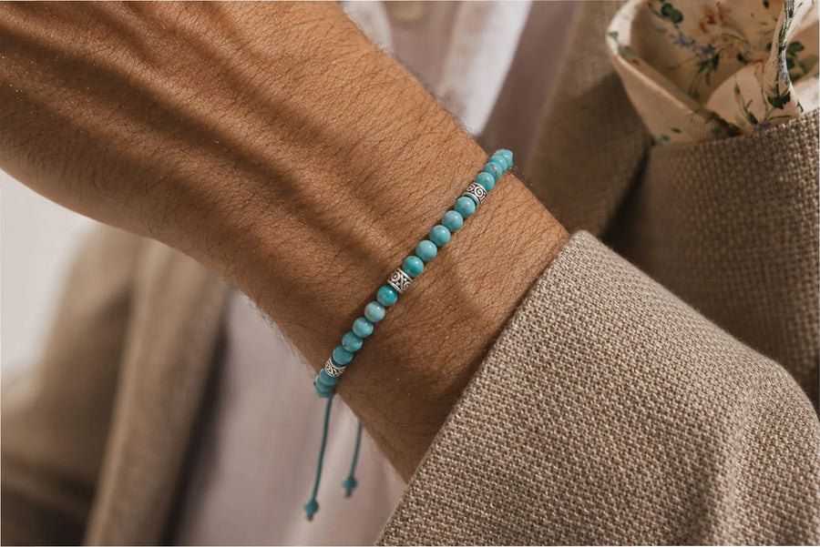 Genuine turquoise bracelet with metal spacers worn on a man’s wrist with a beige textured blazer.
