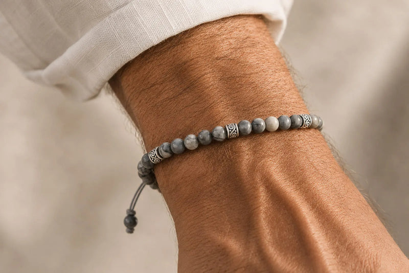 Gray beaded bracelet with natural stone beads and silver details worn on a man’s wrist.