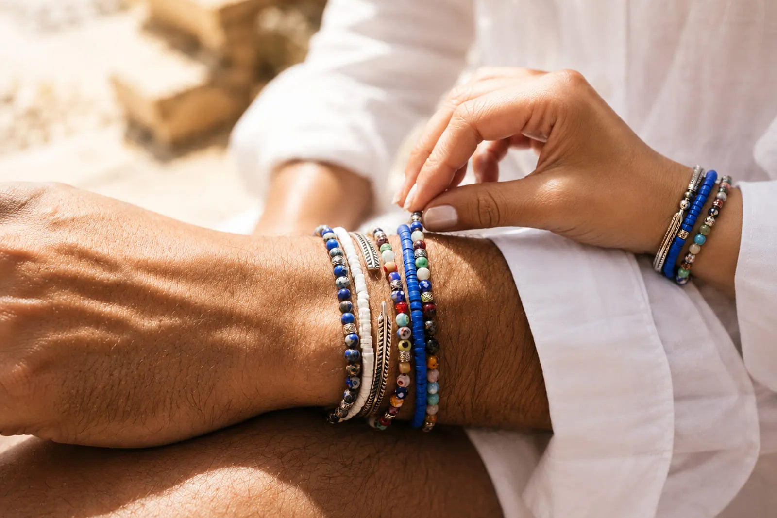His and hers bracelet sets with colorful beads and silver details worn together in a relaxed summer setting.