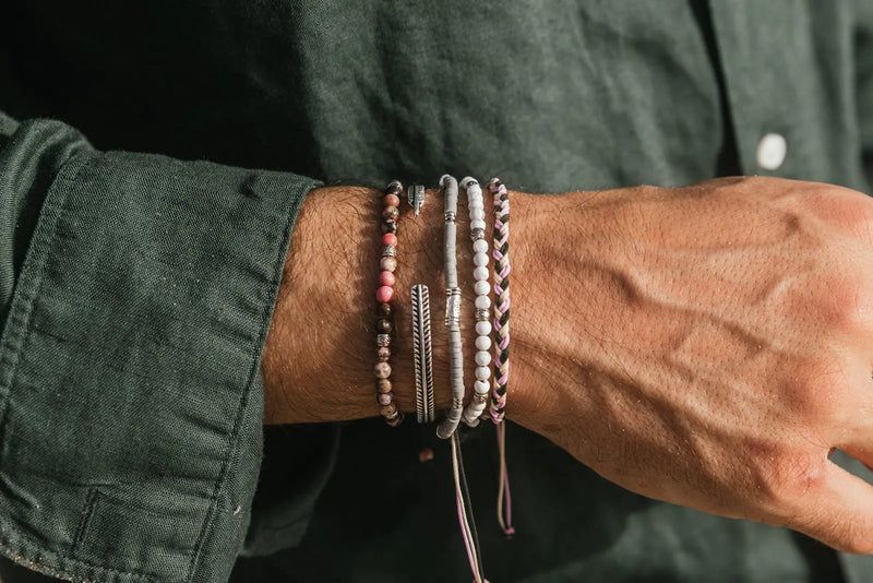 How to stack bracelets for men with a balanced mix of beaded, silver, and woven styles worn with a green shirt.